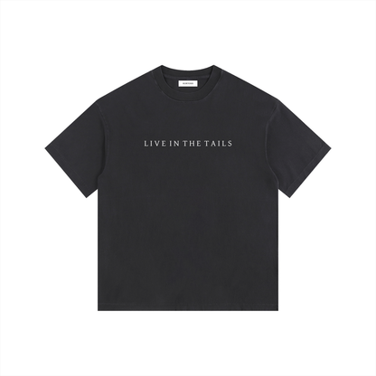Front view of a vintage washed black oversized t-shirt featuring the "Live in the Tails" collection title in minimalist white typography. 260gsm heavyweight cotton with a thick, premium washed finish and drop shoulder silhouette.