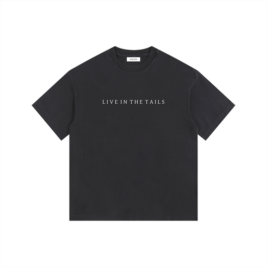 Front view of a vintage washed black oversized t-shirt featuring the "Live in the Tails" collection title in minimalist white typography. 260gsm heavyweight cotton with a thick, premium washed finish and drop shoulder silhouette.